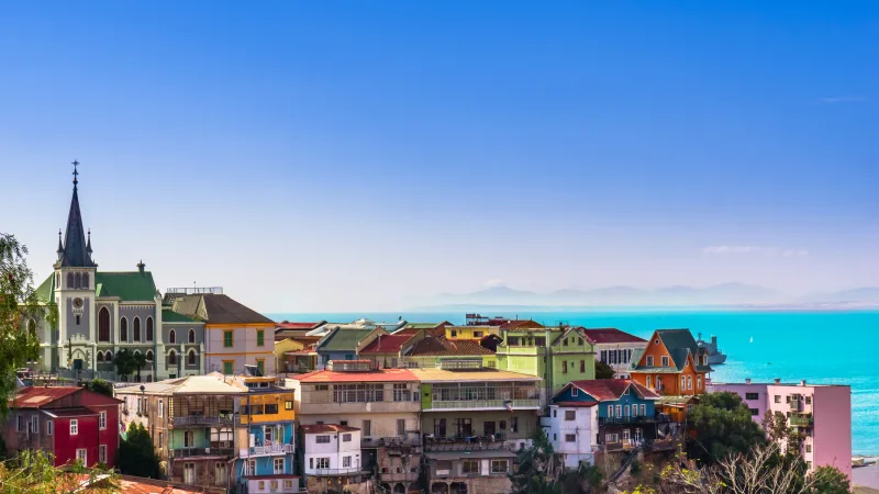 Vista panorâmica de Valparaíso, Chile, com casas coloridas nos morros, uma igreja gótica e o oceano Pacífico ao fundo