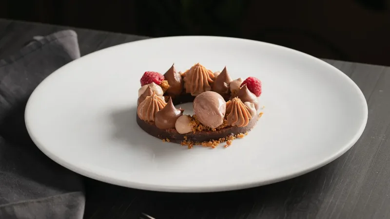 Elegant chocolate tart topped with piped chocolate mousse, fresh raspberries, and cookie crumble on a white plate
