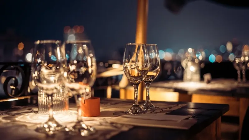 Elegant restaurant table set with empty wine glasses glowing under warm candlelight, with bokeh city lights in the background