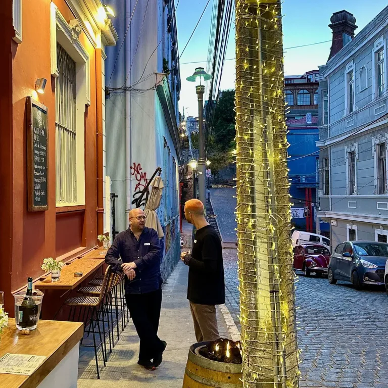 Terraza del bar Corazón Continto en Valparaíso, con dos personas conversando junto a cactus iluminados y una calle empedrada