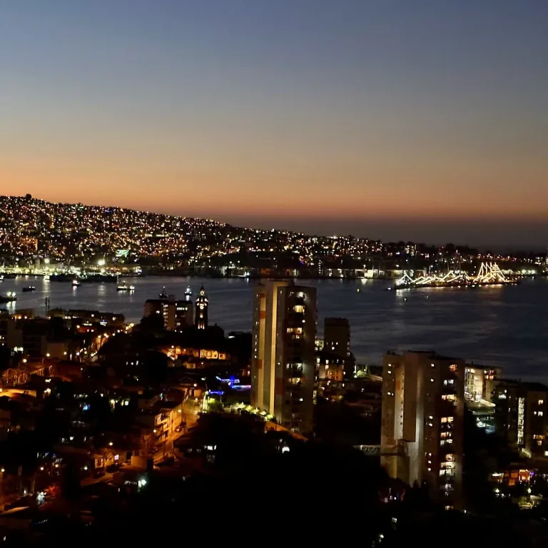 Vista nocturna de Valparaíso con sus cerros iluminados, la bahía y el puerto al atardecer.